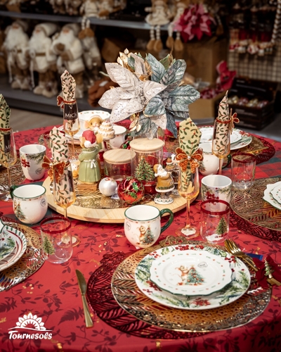 Table de Noël rouge et or avec vaisselle à motifs de sapin, serviettes nouées et poinsettia doré en jardinerie Tournesols